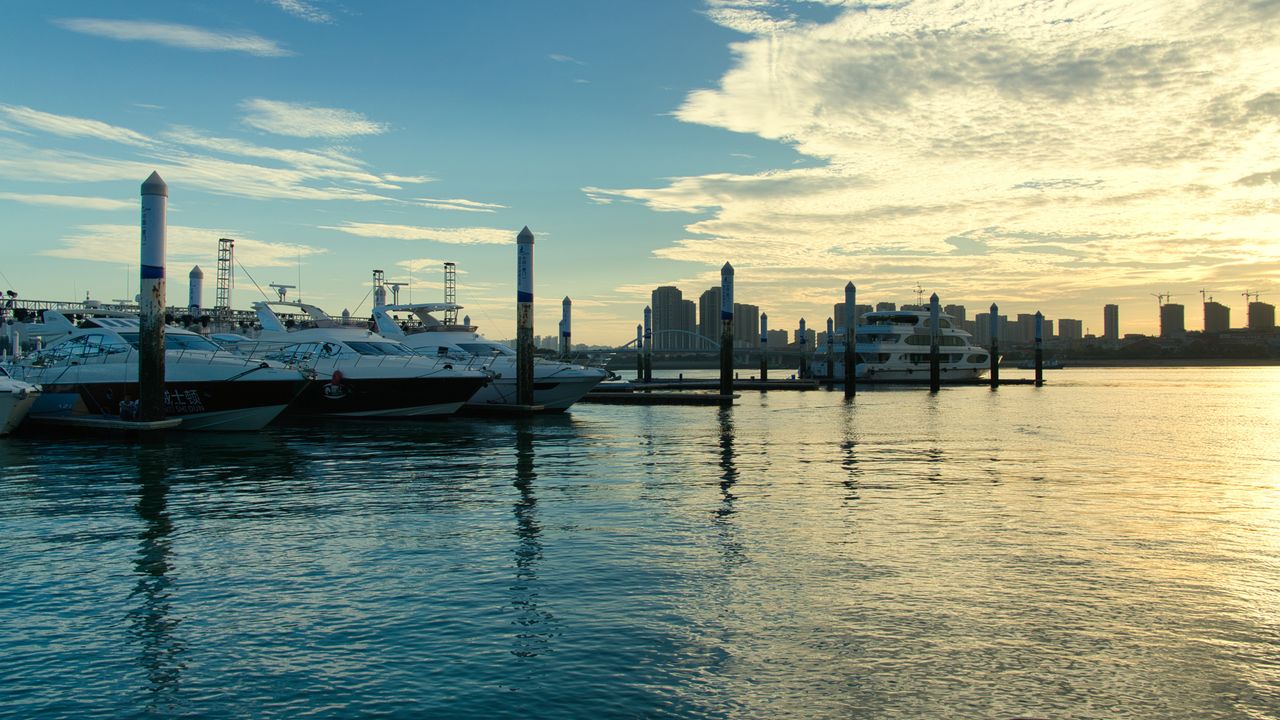 Yachts moored in a marina at twilight, the water reflecting a violet sky